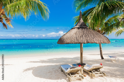 Chairs with umbrella at luxury beach with palms and blue ocean.