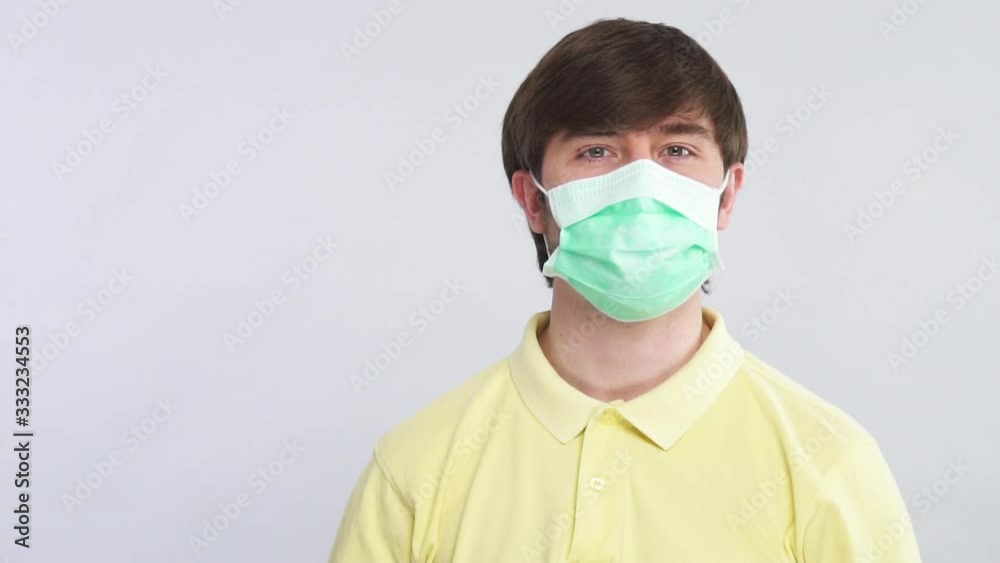 happy man putting on disposable sterile mask to protect his face and shows thumbs up to camera isolated on grey happy man putting on disposable sterile mask to protect his face and shows thumbs up to camera isolated on grey