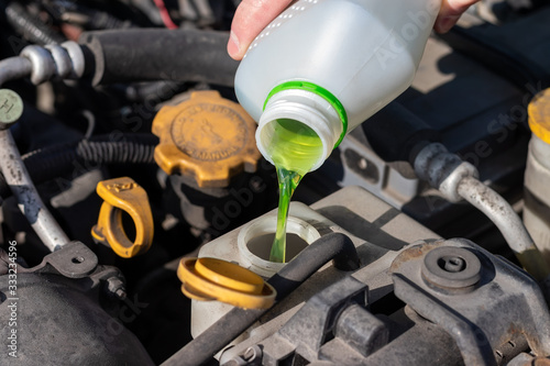 Photography Hand with bottle pouring antifreeze coolant into the expansion tank