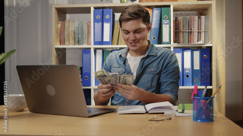 Handsome successful young man surprised getting money banknotes out of notebook making business rejoicing with profits working in office company.