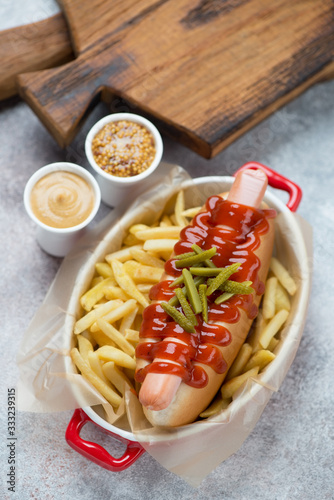 Hot-dog with french fries in a serving bowl, elevated view on a beige stone background with rustic wooden chopping boards