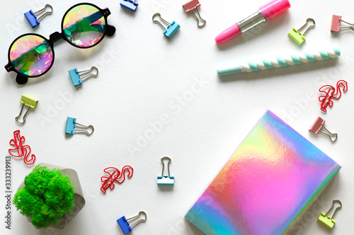 Kaleidoscopic glasses, green fresh mini-moss and coloured pens, multi-coloured mini paper holders, pink flamingo paper clips on a white background. There is a place for text. 