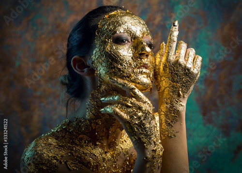 Girl with a mask on her face made of gold leaf. Gloomy studio portrait of a b...