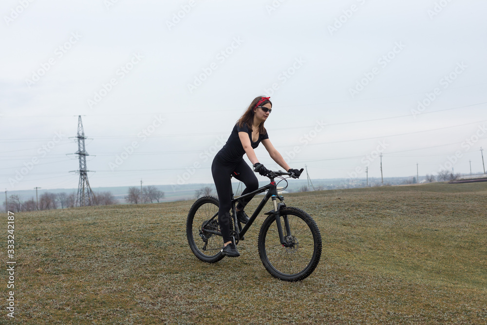 Girl on a mountain bike on offroad, beautiful portrait of a cyclist in rainy weather, Fitness girl rides a modern carbon fiber mountain bike in sportswear. Close-up portrait of a girl in red bandana.