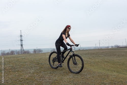 Girl on a mountain bike on offroad, beautiful portrait of a cyclist in rainy weather, Fitness girl rides a modern carbon fiber mountain bike in sportswear. Close-up portrait of a girl in red bandana.