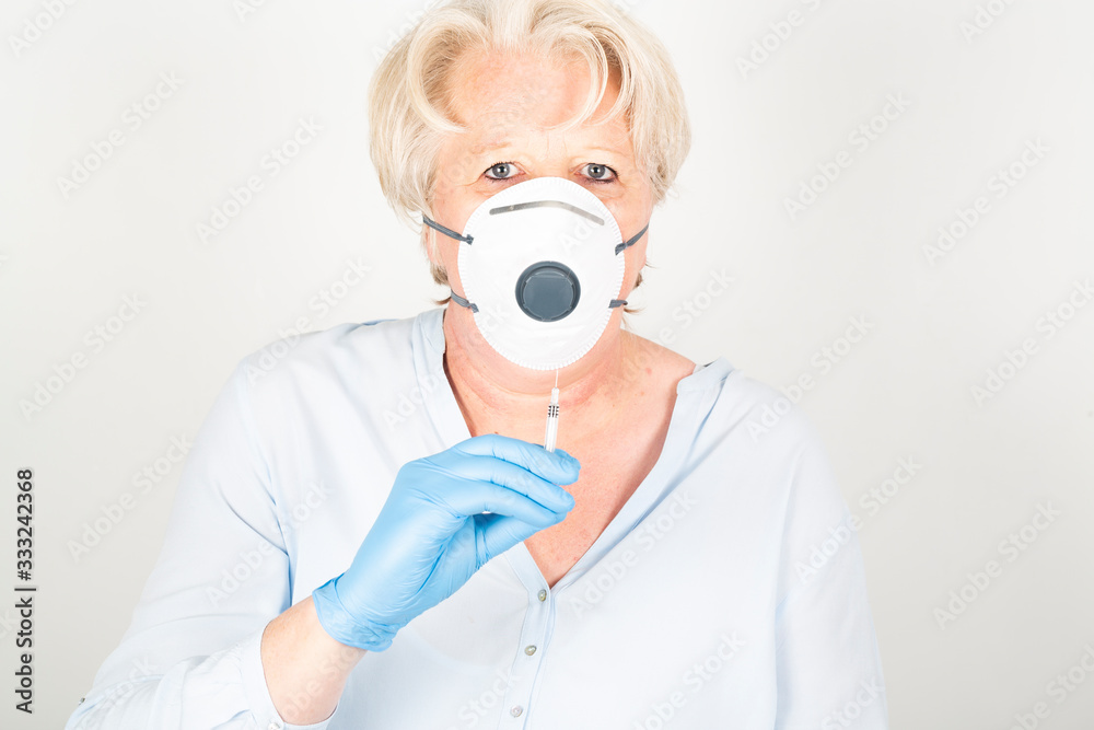 Close-up of a mature caucasian doctor with blond hair wearing a face mask to protect herself from coronavirus infection or air pollution. With syringe Close-up of a mature caucasian doctor with blond hair wearing a face mask to protect herself from coronavirus infection or air pollution. With syringe