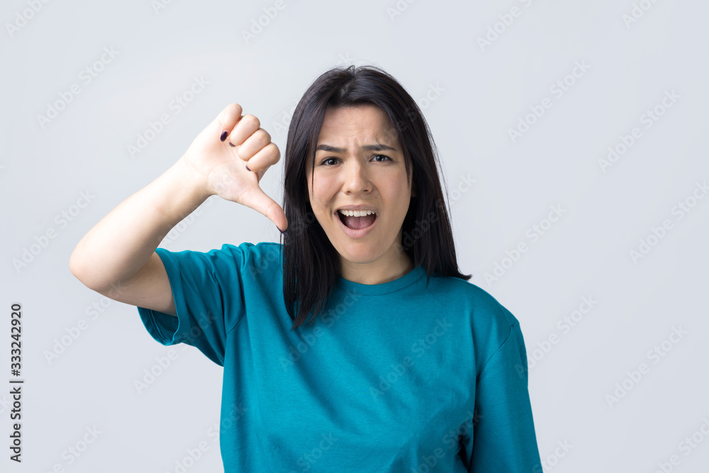 Young brunette in a blue tank top giving thumb down gesture looking with negative expression Young brunette in a blue tank top giving thumb down gesture looking with negative expression