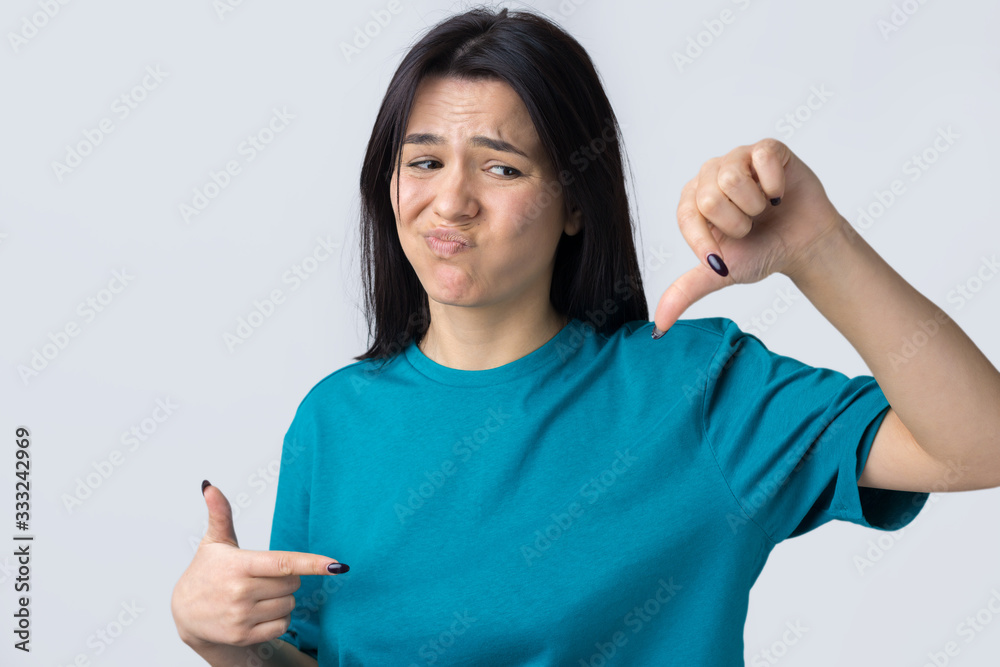 Young brunette in a blue tank top giving thumb down gesture looking with negative expression Young brunette in a blue tank top giving thumb down gesture looking with negative expression