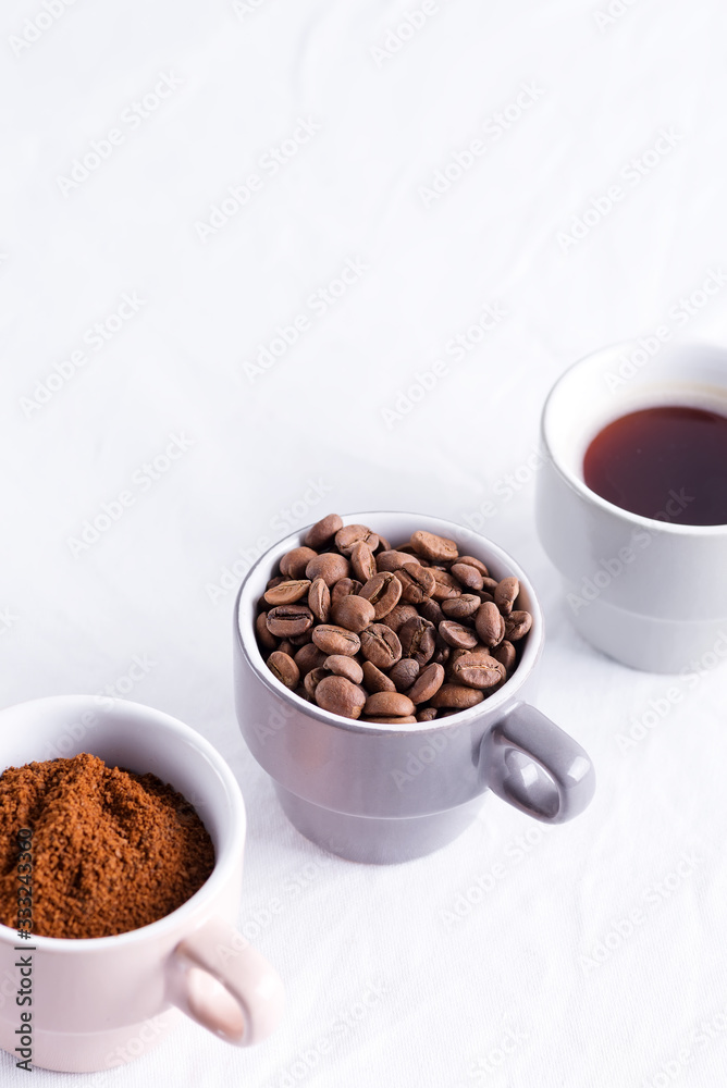 Three cups of different condition of coffee - beans, freshly ground and coffee drink on a marble light grey background. Three cups of different condition of coffee - beans, freshly ground and coffee drink on a marble light grey background.