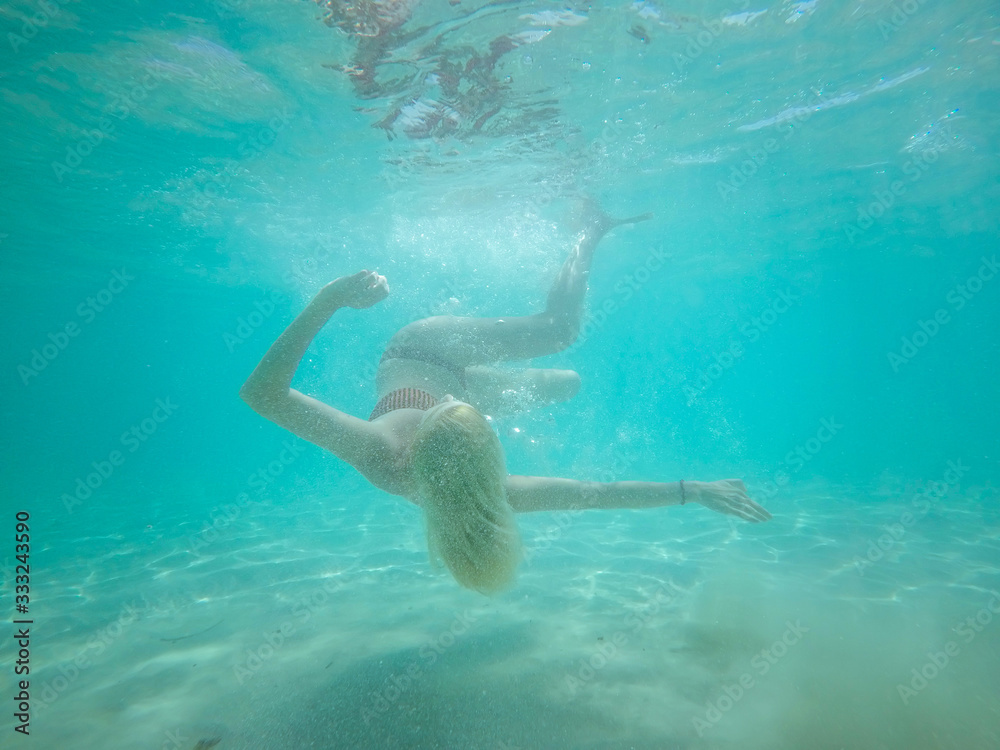 Under water photo of a woman in bikini diving in turquoise sea w