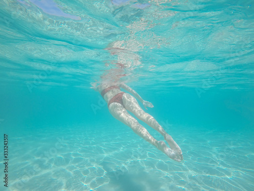 Rear underwater view of women body swimming under turquoise wate