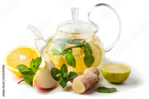 isolated glass transparent teapot with tea from ginger root, lime, orange, apple, mint on a white background