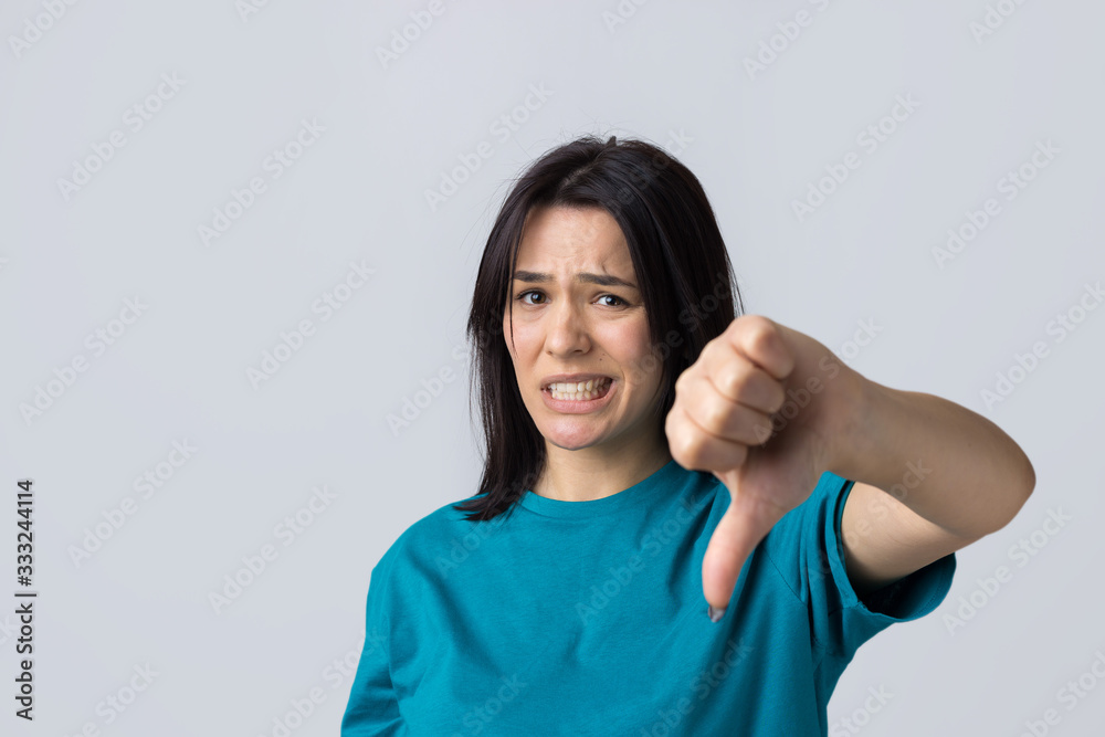 Young brunette in a blue tank top giving thumb down gesture looking with negative expression Young brunette in a blue tank top giving thumb down gesture looking with negative expression