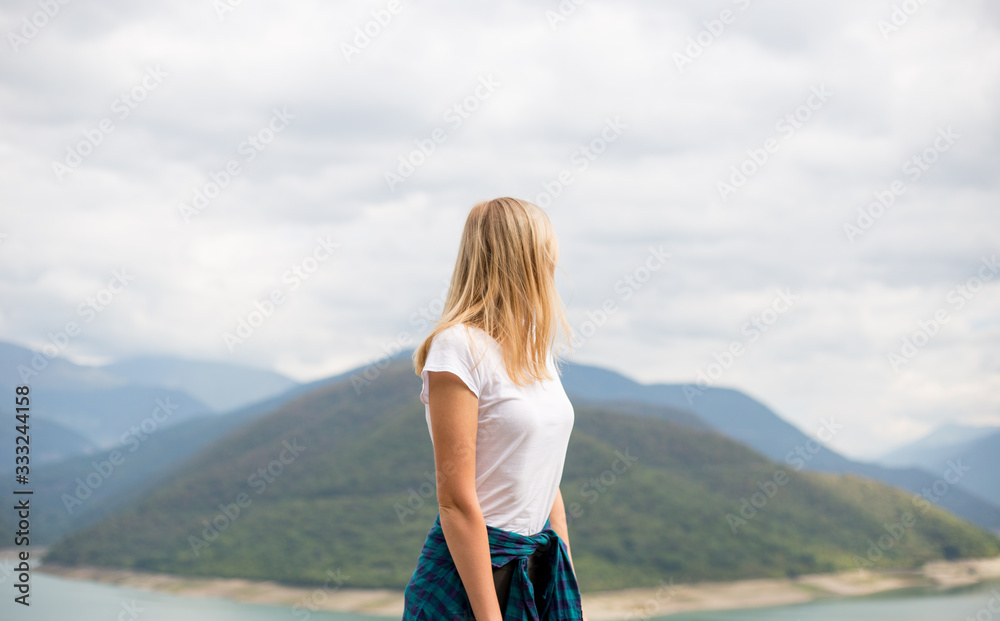 Happy blonde woman stands on the background of mountain peaks. Ecotourism, travel concept and discovery of beautiful places