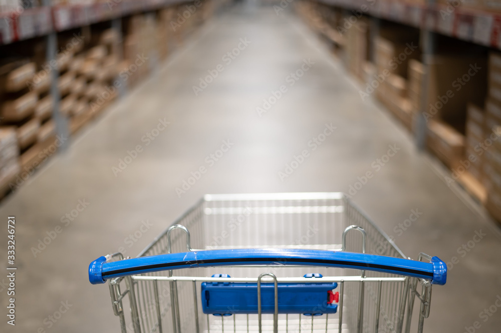Empty shopping cart in a furniture store warehouse. Supermarket shopping basket aisle with box shelf abstract blur defocused background