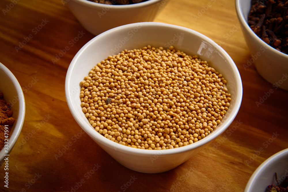 Yellow mustard seeds in white bowl on wooden background Yellow mustard seeds in white bowl on wooden background