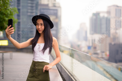 Young beautiful Asian tourist woman taking selfie against view of the city © Ranta Images