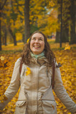 Woman throwing autumn leaves in theair in romantic forest. Cute brunette playing with leaves in the woods. Romantic autumn photo.