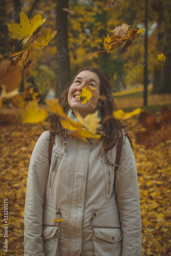 Woman throwing autumn leaves in theair in romantic forest. Cute brunette playing with leaves in the woods. Romantic autumn photo. photo
