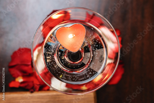 Burning candle in the shape of a heart, in a transparent glass  with drops