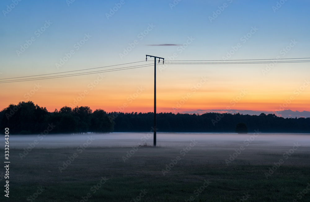 Electricity Pylon with Power Lines in the Middle of a Field against the Background of Evening Fog and Haze at Sunset
