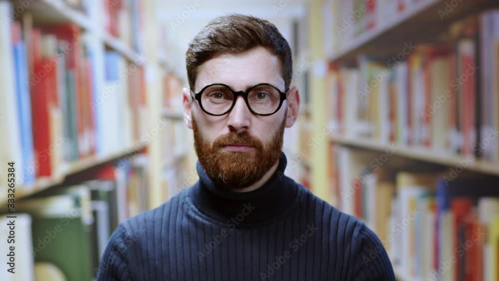 Indoor portrait bearded young man librarian or student wearing glasses keeping order in the library. Isolated on background. People and education concept. Indoor portrait bearded young man librarian or student wearing glasses keeping order in the library. Isolated on background. People and education concept.
