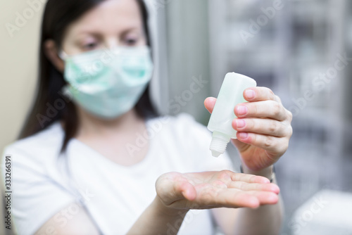 Young woman wearing protective medical mask while applying hand sanitizer