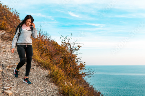 A young woman with a backpack on her back descends a rocky slope. In the background, the sea and the sky. Copy space. Concept of Hiking and outdoor activities
