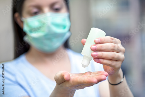 Young woman wearing protective medical mask while applying hand sanitizer