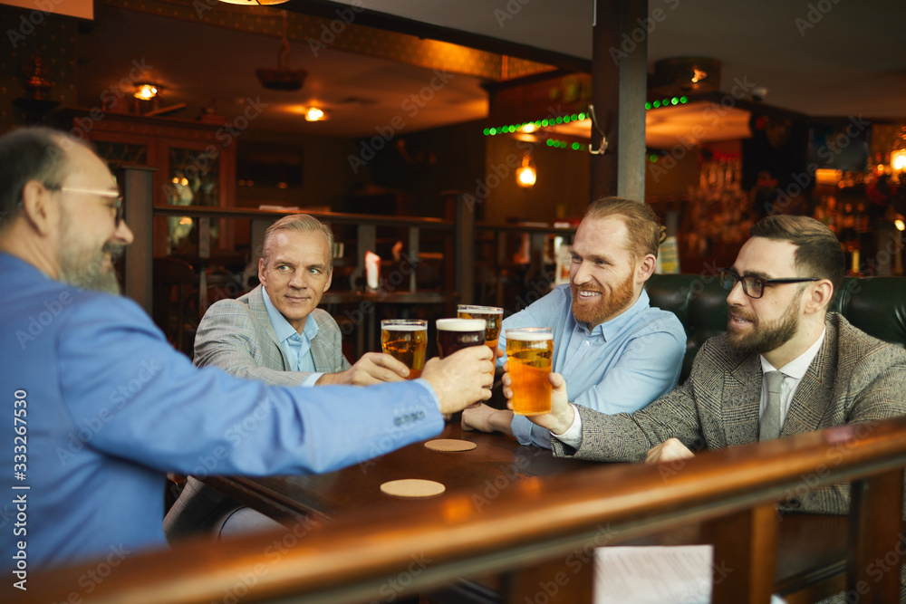 Group of business colleagues toasting with glasses of beer and have a funny time they resting after hard work in cafe