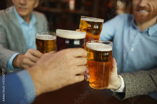 Close-up of group of men holding glasses with beer and celebrating during meeting in cafe