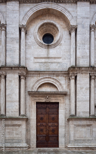 Facade of a romanesque italian church with wooden carved portal and many white columns.