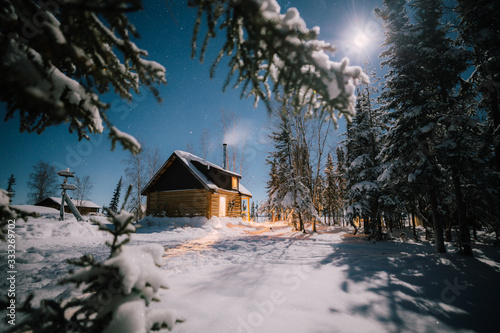 Cozy wooden log cabin in the woods at winter moonlight night with the smoking chimney