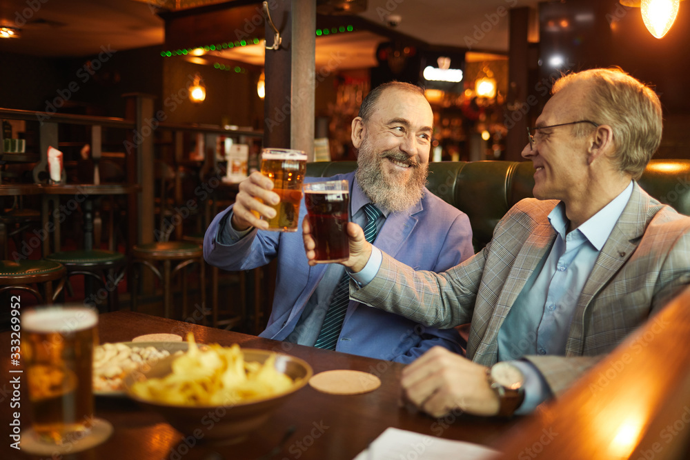 Two senior men drinking beer and talking to each other while resting after work in the bar