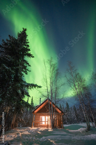 A cozy warm cabin with the warm light in the snowy forest under the northern lights, Yellowknife, Northwest Territories, Canada, North America