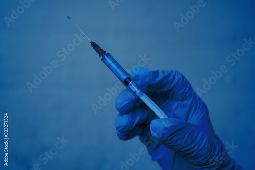 A hand in a medical glove holds a syringe. Dark background.