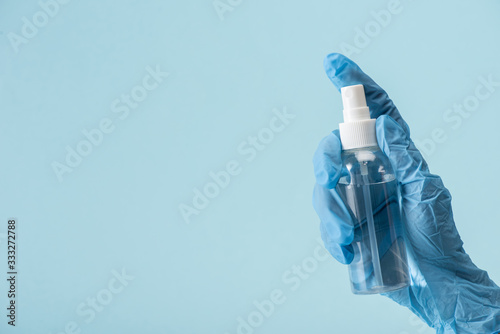cropped view of doctor in latex glove holding bottle with hand sanitizer isolated on blue