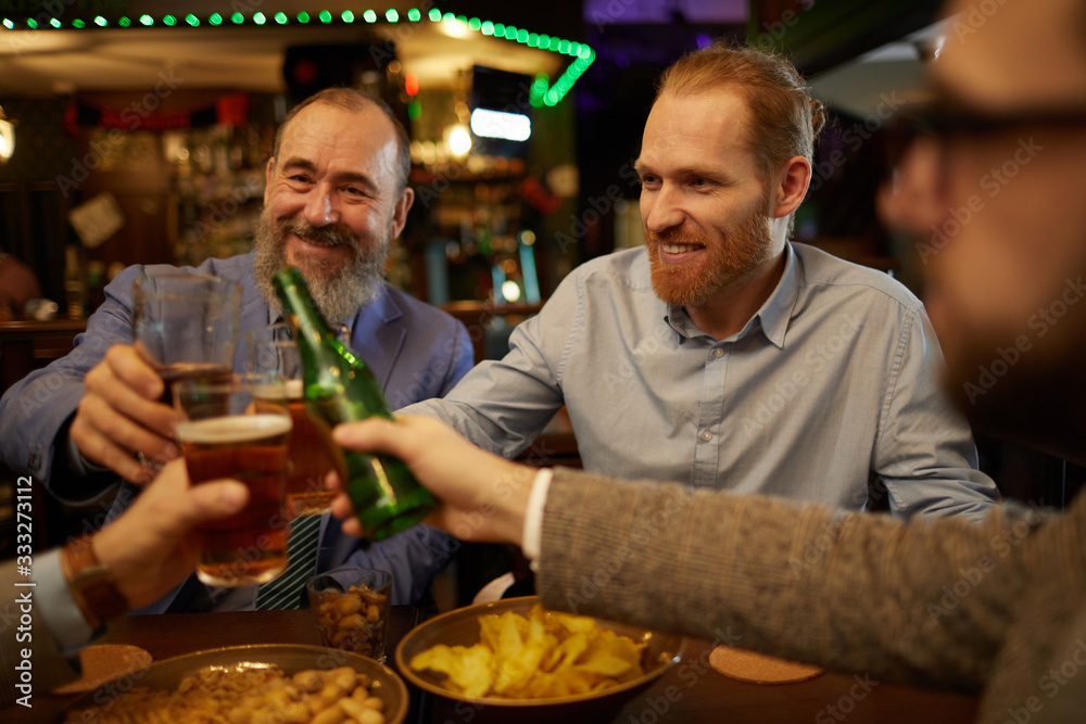 Happy bearded men toasting with beer and having fun after work day in the pub