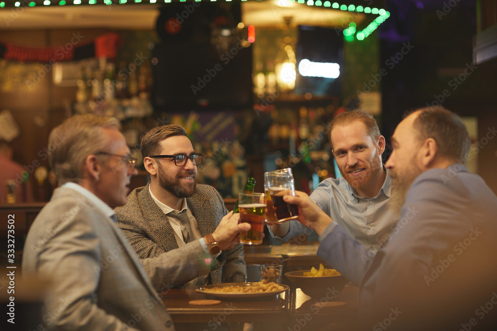 Group of businessmen holding glasses of beer and discussing some working moments in informal setting in the pub Group of businessmen holding glasses of beer and discussing some working moments in informal setting in the pub