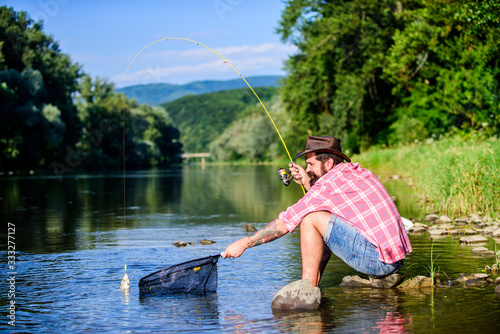 hipster fishing with spoon-bait. successful fisherman in lake water. fly fish hobby of man. Hipster in checkered shirt. big game fishing. relax on nature. Nice day for fishing. man with fish on rod