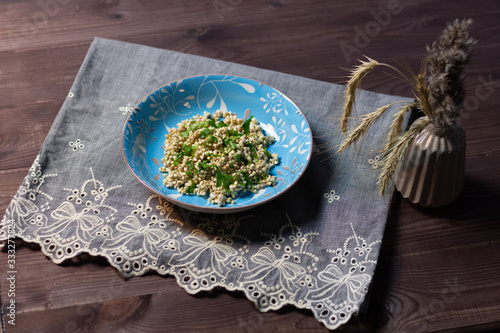 soaked green buckwheat  in blue bowl with parsley on table cloth on brown wooden background and vase with spikes