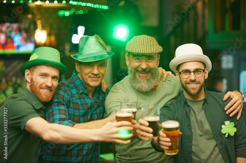 Portrait of group of friends wearing hats and toasting with beer while smiling at camera and celebrating the holiday