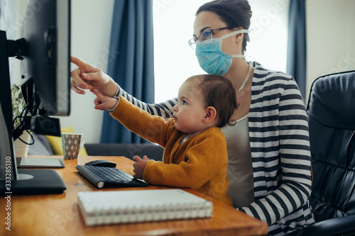 Young mother working with her baby on computer at her home office. photo