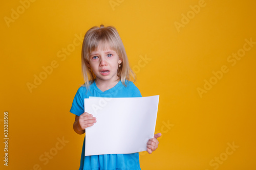 baby girl with an empty sheet of paper crying, upset on a yellow background