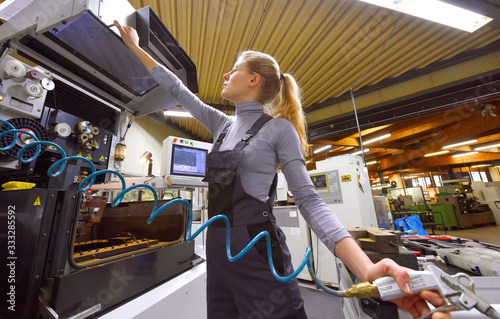 A young woman works as a computerized  numerical control technician. She is seen at her workplace wearing a blue overall. 
