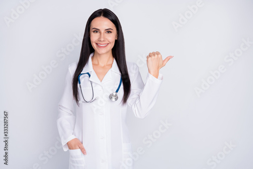 Photo of beautiful doctor lady good mood smiling patients direct thumb finger empty space insurance offer wear white lab coat stethoscope isolated grey color background