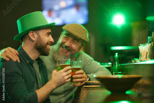 Two happy men in hats talking to each other laughing and drinking beer at the bar counter in pub
