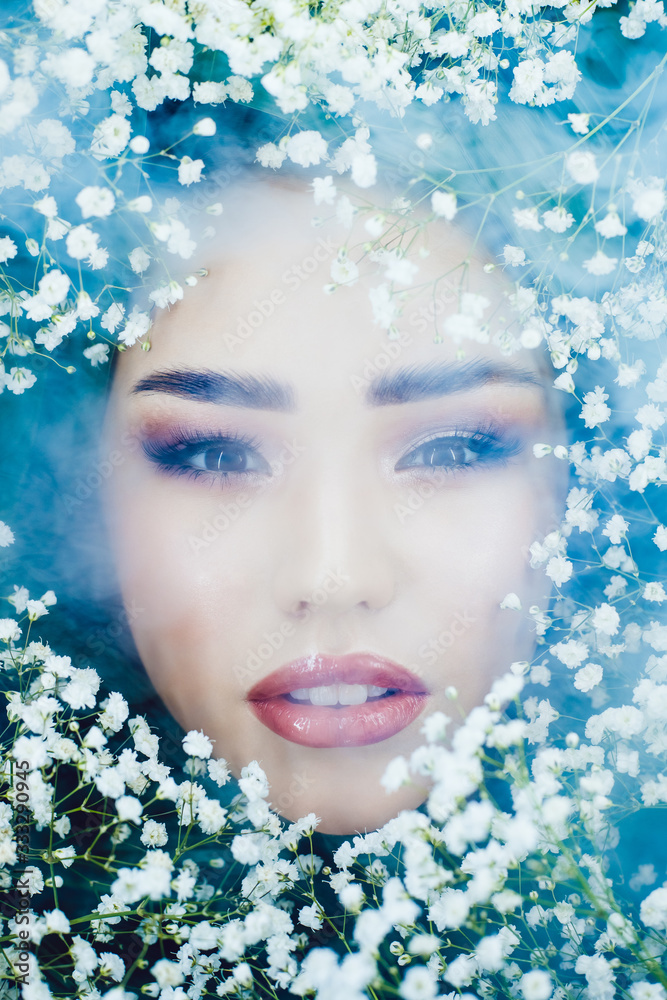 Portrait of beautiful girl in smoke with small white flowers around her face. Woman and flowers. Spring.