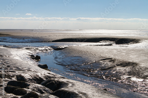 the Wadden Sea with a pronounced tideway at low tide on the North Sea Germany with backlight and a view to the horizon line