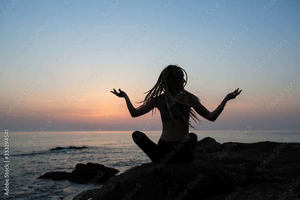 Silhouette of a yoga woman on the evening ocean.